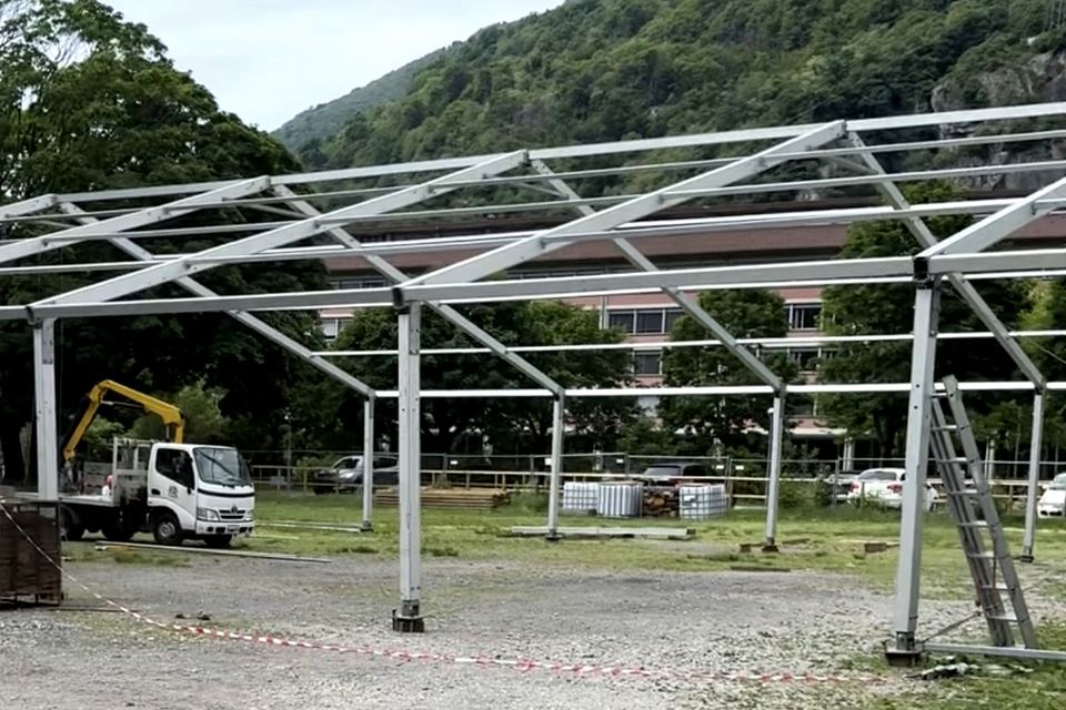 Telaio in acciaio di una tensostruttura ER Noleggio ancora senza telo, con autocarro con gru e montagne boscose dietro
