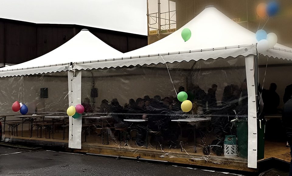 Due pagode unite con pareti trasparenti e palloncini colorati durante l'inaugurazione di un negozio, con persone sedute dentro