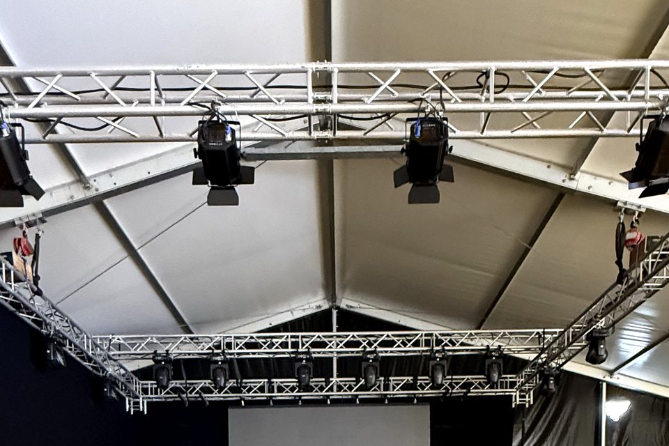 Palco rialzato dentro una tensostruttura, con traliccio, fari, schermo bianco e pavimento in legno