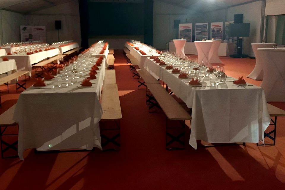 Cena di gala in tensostruttura con lunghe tavolate, tovaglie bianche, tovaglioli rossi e moquette rossa